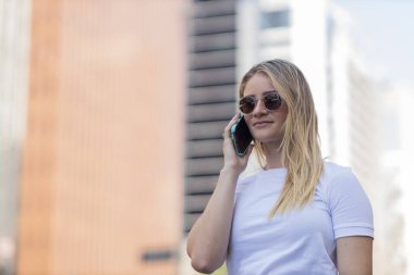 Gündüz vakti arka planda şehir manzarası olan akıllı telefon kullanan genç bir kadın. Yüksek kalite fotoğraf. Cep telefonu, teknoloji, şehir kavramı. 