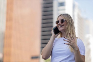 Gündüz vakti arka planda şehir manzarası olan akıllı telefon kullanan genç bir kadın. Yüksek kalite fotoğraf. Cep telefonu, teknoloji, şehir kavramı. 