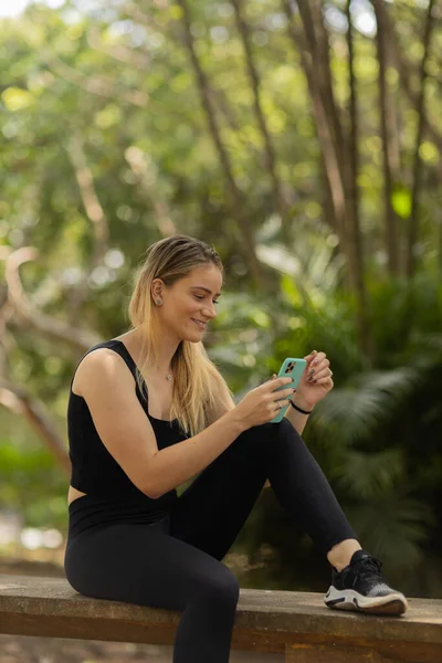 Gündüz vakti arka planda yeşil park olan akıllı telefon kullanan genç bir kadın. Yüksek kalite fotoğraf. Cep telefonu, teknoloji, şehir konsepti. Yüksek kalite fotoğraf