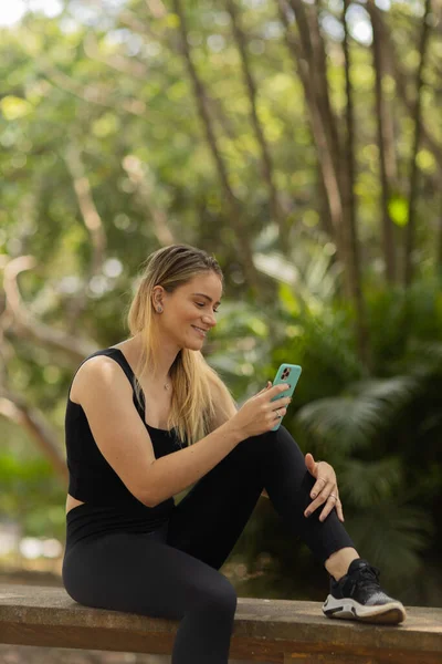 Gündüz vakti arka planda yeşil park olan akıllı telefon kullanan genç bir kadın. Yüksek kalite fotoğraf. Cep telefonu, teknoloji, şehir konsepti. Yüksek kalite fotoğraf