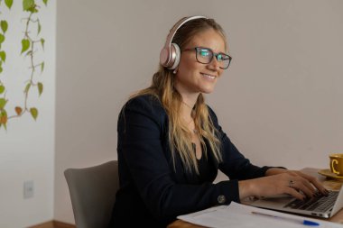 Evde dizüstü bilgisayar, masa ve kulaklıklarla çalışan genç bir kadın. Merkez ofis konsepti. Çalışmak için gri defter. Yüksek kalite fotoğraf