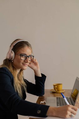 Evde dizüstü bilgisayar, masa ve kulaklıklarla çalışan genç bir kadın. Merkez ofis konsepti. Çalışmak için gri defter. Yüksek kalite fotoğraf