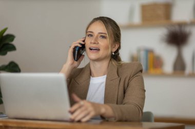 Evde dizüstü bilgisayarı ve kağıtları olan genç bir kadın yatak odasında cep telefonuyla konuşuyor. Merkez ofis konsepti. Çalışmak için gri defter. Yüksek kalite fotoğraf