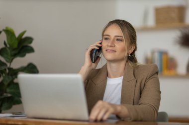 Evde dizüstü bilgisayarı ve kağıtları olan genç bir kadın yatak odasında cep telefonuyla konuşuyor. Merkez ofis konsepti. Çalışmak için gri defter. Yüksek kalite fotoğraf