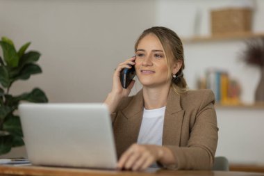 Evde dizüstü bilgisayarı ve kağıtları olan genç bir kadın yatak odasında cep telefonuyla konuşuyor. Merkez ofis konsepti. Çalışmak için gri defter. Yüksek kalite fotoğraf