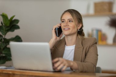 Evde dizüstü bilgisayarı ve kağıtları olan genç bir kadın yatak odasında cep telefonuyla konuşuyor. Merkez ofis konsepti. Çalışmak için gri defter. Yüksek kalite fotoğraf