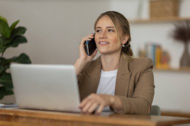 Evde dizüstü bilgisayarı ve kağıtları olan genç bir kadın yatak odasında cep telefonuyla konuşuyor. Merkez ofis konsepti. Çalışmak için gri defter. Yüksek kalite fotoğraf