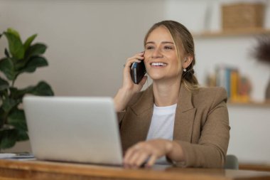Evde dizüstü bilgisayarı ve kağıtları olan genç bir kadın yatak odasında cep telefonuyla konuşuyor. Merkez ofis konsepti. Çalışmak için gri defter. Yüksek kalite fotoğraf