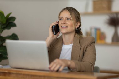 Evde dizüstü bilgisayarı ve kağıtları olan genç bir kadın yatak odasında cep telefonuyla konuşuyor. Merkez ofis konsepti. Çalışmak için gri defter. Yüksek kalite fotoğraf