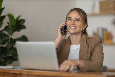Evde dizüstü bilgisayarı ve kağıtları olan genç bir kadın yatak odasında cep telefonuyla konuşuyor. Merkez ofis konsepti. Çalışmak için gri defter. Yüksek kalite fotoğraf