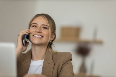Evde dizüstü bilgisayarı ve kağıtları olan genç bir kadın yatak odasında cep telefonuyla konuşuyor. Merkez ofis konsepti. Çalışmak için gri defter. Yüksek kalite fotoğraf