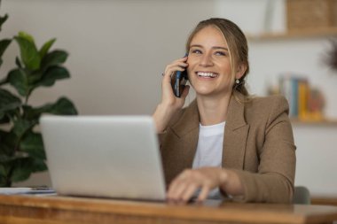 Evde dizüstü bilgisayarı ve kağıtları olan genç bir kadın yatak odasında cep telefonuyla konuşuyor. Merkez ofis konsepti. Çalışmak için gri defter. Yüksek kalite fotoğraf