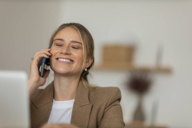 Evde dizüstü bilgisayarı ve kağıtları olan genç bir kadın yatak odasında cep telefonuyla konuşuyor. Merkez ofis konsepti. Çalışmak için gri defter. Yüksek kalite fotoğraf