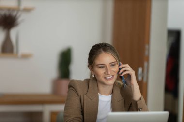 Evde dizüstü bilgisayarı ve kağıtları olan genç bir kadın yatak odasında cep telefonuyla konuşuyor. Merkez ofis konsepti. Çalışmak için gri defter. Yüksek kalite fotoğraf