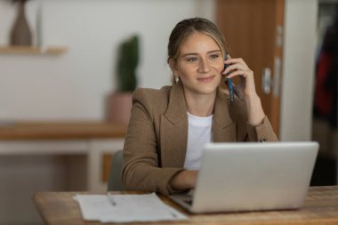 Evde dizüstü bilgisayarı ve kağıtları olan genç bir kadın yatak odasında cep telefonuyla konuşuyor. Merkez ofis konsepti. Çalışmak için gri defter. Yüksek kalite fotoğraf