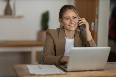 Evde dizüstü bilgisayarı ve kağıtları olan genç bir kadın yatak odasında cep telefonuyla konuşuyor. Merkez ofis konsepti. Çalışmak için gri defter. Yüksek kalite fotoğraf