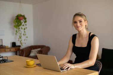 Mutfakta dizüstü bilgisayarı ve mutfak masasında kağıtlarıyla çalışan genç bir kadın. Merkez ofis konsepti. Çalışmak için gri defter. Merkez ofis konsepti. Yüksek kalite fotoğraf