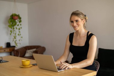 Mutfakta dizüstü bilgisayarı ve mutfak masasında kağıtlarıyla çalışan genç bir kadın. Merkez ofis konsepti. Çalışmak için gri defter. Merkez ofis konsepti. Yüksek kalite fotoğraf