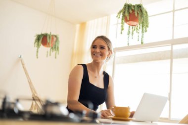 Mutfakta dizüstü bilgisayarı ve mutfak masasında kağıtlarıyla çalışan genç bir kadın. Merkez ofis konsepti. Çalışmak için gri defter. Merkez ofis konsepti. Yüksek kalite fotoğraf