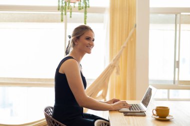 Mutfakta dizüstü bilgisayarı ve mutfak masasında kağıtlarıyla çalışan genç bir kadın. Merkez ofis konsepti. Çalışmak için gri defter. Merkez ofis konsepti. Yüksek kalite fotoğraf