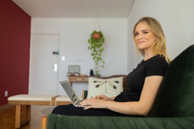 Oturma odasındaki kanepede dizüstü bilgisayarıyla çalışan genç bir kadın. Merkez ofis konsepti. Çalışmak için gri defter. Merkez ofis konsepti. Yüksek kalite fotoğraf