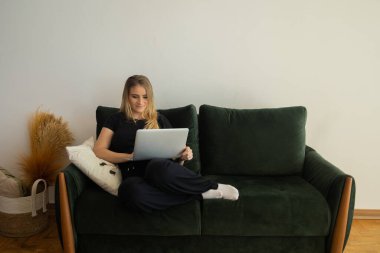 Oturma odasındaki kanepede dizüstü bilgisayarıyla çalışan genç bir kadın. Merkez ofis konsepti. Çalışmak için gri defter. Merkez ofis konsepti. Yüksek kalite fotoğraf