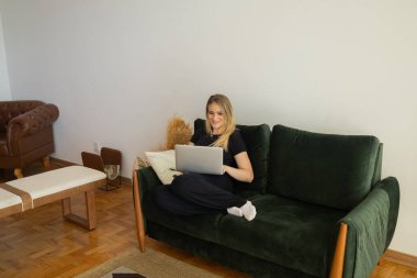 Oturma odasındaki kanepede dizüstü bilgisayarıyla çalışan genç bir kadın. Merkez ofis konsepti. Çalışmak için gri defter. Merkez ofis konsepti. Yüksek kalite fotoğraf