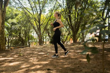 Genç bir kadın parkta koşuyor ve koşuyor. Spor yaparken bayan sporcu. İyi, sağlıklı bir konsept. Yüksek kalite fotoğraf