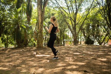 Genç bir kadın parkta koşuyor ve koşuyor. Spor yaparken bayan sporcu. İyi, sağlıklı bir konsept. Yüksek kalite fotoğraf