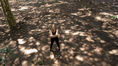 Genç bir kadın parktaki antrenmandan önce esneme hareketleri yapıyor. Sporcu kadın spora hazırlanıyor. İHA görüntüsü. İyi, sağlıklı bir konsept. Yüksek kalite çekim