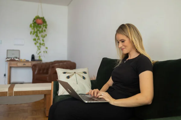 Young woman working at home from her living room couch with laptop on her lap. Home office concept. Gray notebook for working. Home office concept. High quality photo