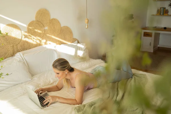 年轻的女人在卧室里干活 床上有笔记本电脑 女人躺下 总部概念 用于工作的灰色笔记本 舒服舒适 总部概念 高质量的照片 — 图库照片