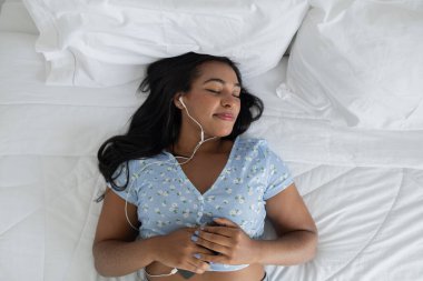 Genç siyahi kadın yatağında evinde kulaklıkla müzik dinliyor. İyi bir konsept, mutlu. Yüksek kalite fotoğraf. 