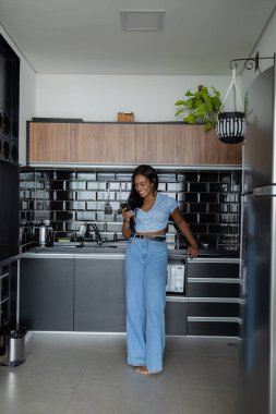 Genç siyahi bir kadın evinin mutfağında akıllı telefonuyla çalışıyor. Merkez ofis kavramı. 