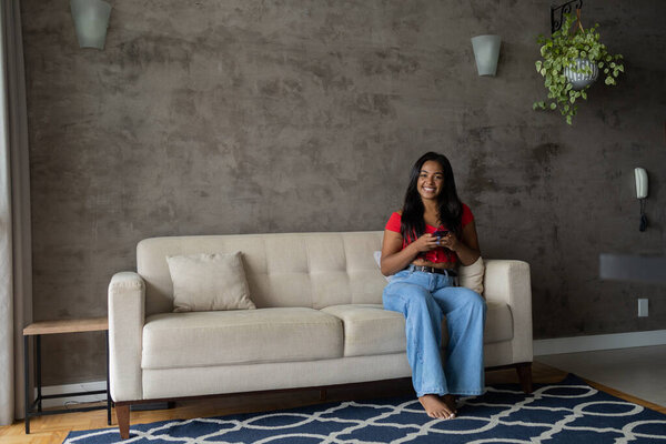 Young black woman working at home with smartphone sitting on her couch in the living room.  Home office concept. High quality photo