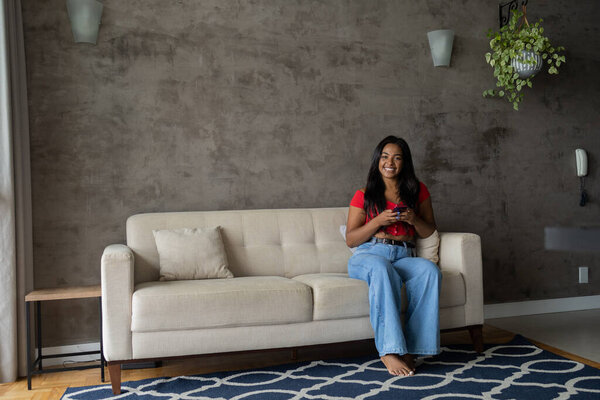 Young black woman working at home with smartphone sitting on her couch in the living room.  Home office concept. High quality photo