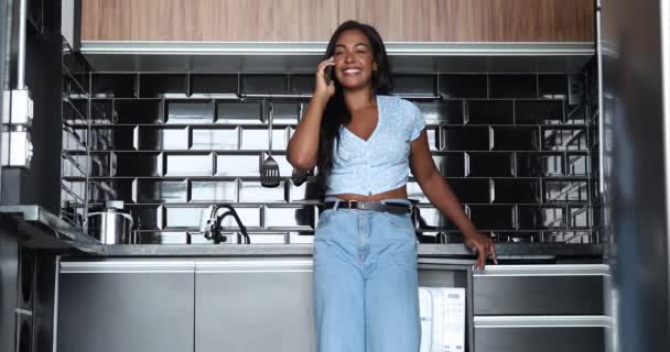 アパートのキッチンでスマホを持って家で働いている若い黒人女性 ホームオフィスのコンセプト — ストック動画