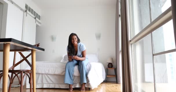 若い黒人女性が家で働いていて スマートフォンが寝室のベッドの上に座っている ホームオフィスのコンセプト — ストック動画