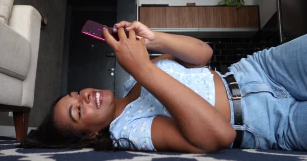 自宅でスマホを持って働く若い黒人女性がキッチンリビングルームのオフィスコンセプトに横になっています 高品質ビデオ — ストック動画