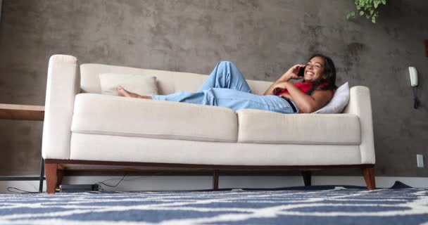 自宅でスマホを持って働く若い黒人女性がリビングのソファに横になっている 内務省の概念 高品質ビデオ — ストック動画