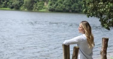 Gündüz vakti arka planda yeşil park olan akıllı telefon kullanan genç beyaz bir kadın. Su, göl. Yüksek kaliteli video. Cep telefonu, teknoloji, şehir kavramı.