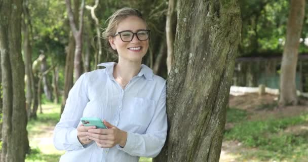 Mujer Blanca Joven Usando Teléfono Inteligente Durante Día Con Parque — Vídeo de stock