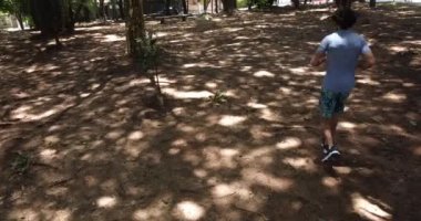 Genç adam arka planda yeşil bir parkla gündüz koşuyor.