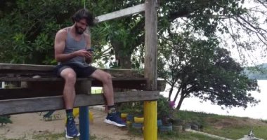 Genç adam, arka planda yeşil parkı olan akıllı telefon kullanıyor.