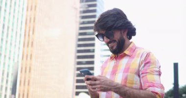 Arka planda şehir manzaralı akıllı telefon kullanan genç bir adam görüntüsü.