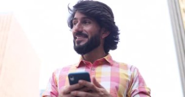 Arka planda şehir manzaralı akıllı telefon kullanan genç bir adam görüntüsü.