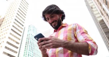 Arka planda şehir manzaralı akıllı telefon kullanan genç bir adam görüntüsü.