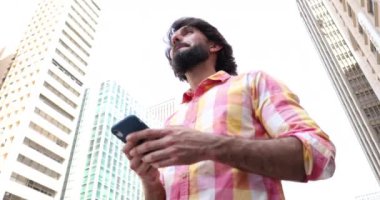 Arka planda şehir manzaralı akıllı telefon kullanan genç bir adam görüntüsü.