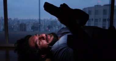 Genç bir adam, arka planda şehir manzarası olan balkonunda gece vakti uzanan akıllı bir telefon kullanıyor..