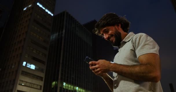 背景に都会の風景を背景に 夜にスマートフォンを使う若者の姿 — ストック動画